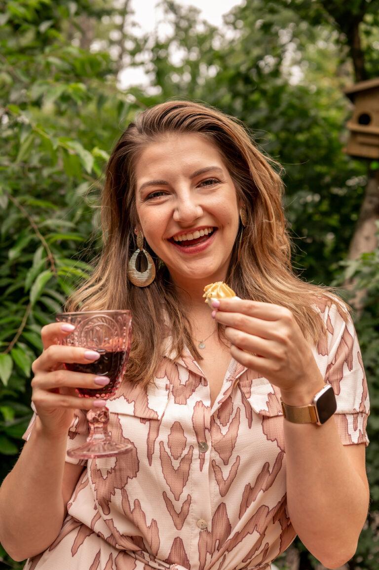 Simone den Hartog lachend met een wijntje en borrelhapje in haar hand